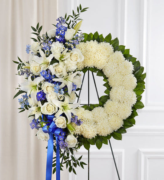 Serene Blessings Wreath in Blue and White, funeral standing wreath with white roses, blue delphinium, chrysanthemums, and a blue ribbon