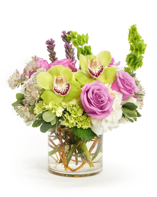 Vibrant floral arrangement featuring orchids, roses, and lush greenery in a clear glass vase.