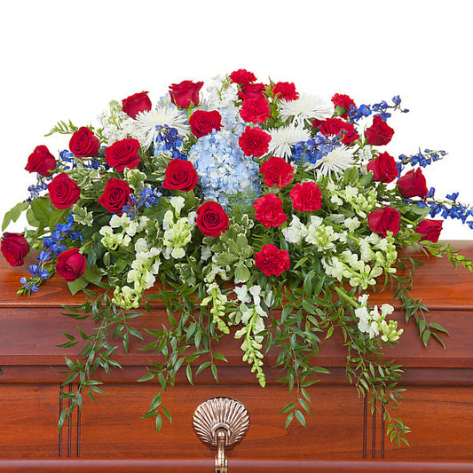 Honor Casket Spray, half casket spray with red roses, red carnations, blue hydrangeas, blue delphinium, white chrysanthemums, and mixed white flowers accented with greenery