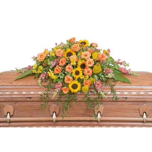 Heaven's Sunset Casket Spray, full casket spray with coral roses, sunflowers, and mixed pink and yellow flowers accented with greenery